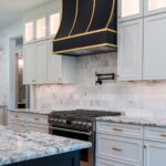 bright, traditional kitchen with black and warm neutrals featuring a black Hoodsly sloped hood with brass strapping