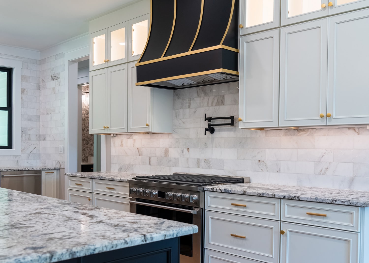 bright, traditional kitchen with black and warm neutrals featuring a black Hoodsly sloped hood with brass strapping